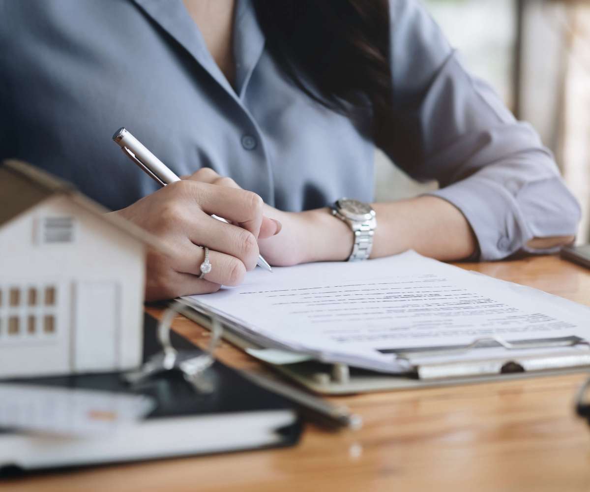registre des mandats immobiliers - un agent immobilier remplissant des documents à son bureau devant une maison miniature
