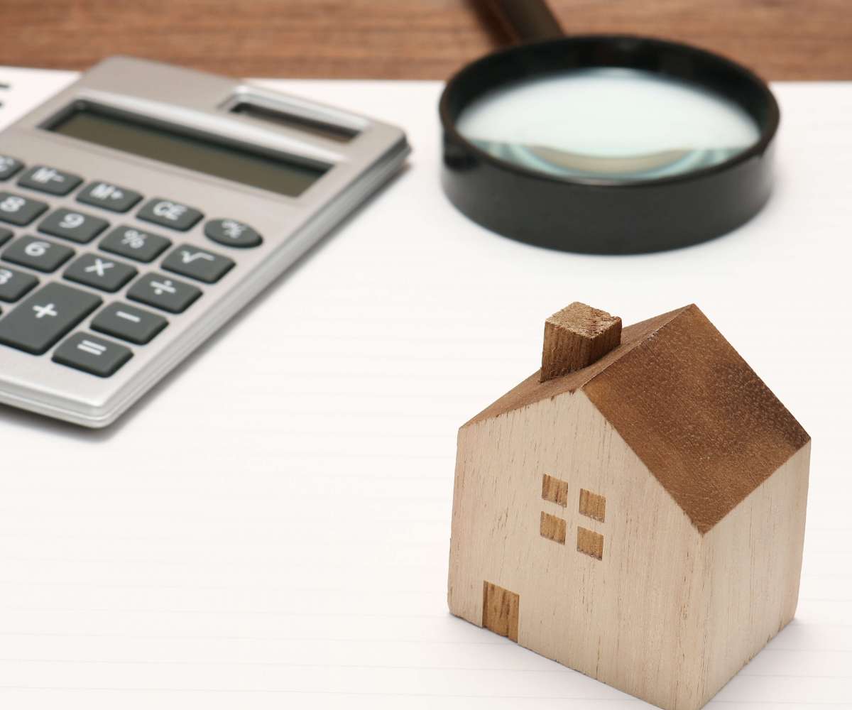 vae immobilier - une maison miniature en bois, une loupe et une calculette posées sur un bureau